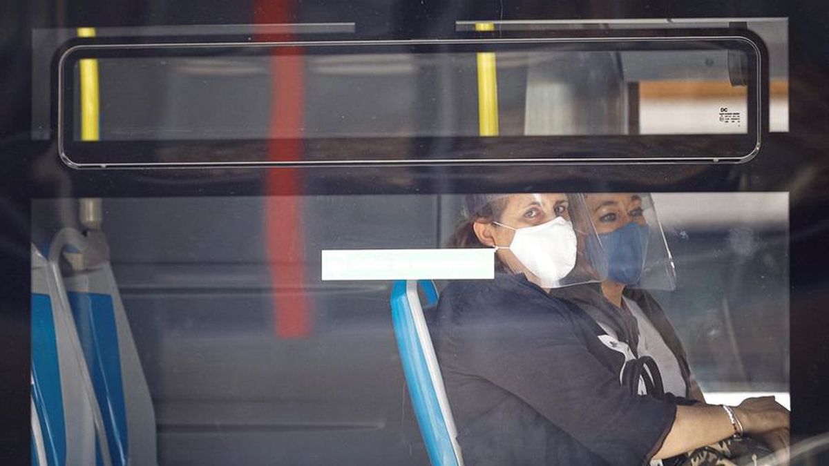 Dos mujeres con mascarilla y pantalla se sientan al lado en un autobús de la EMT en Madrid