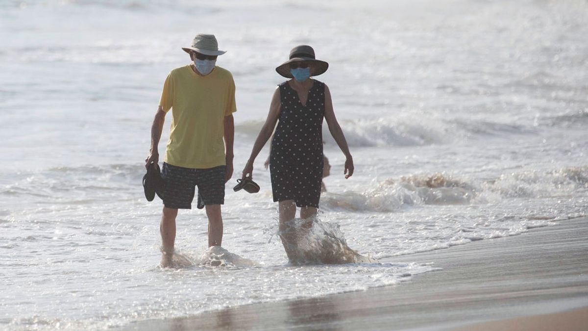 Dos personas pasean por una playa de California con mascarillas