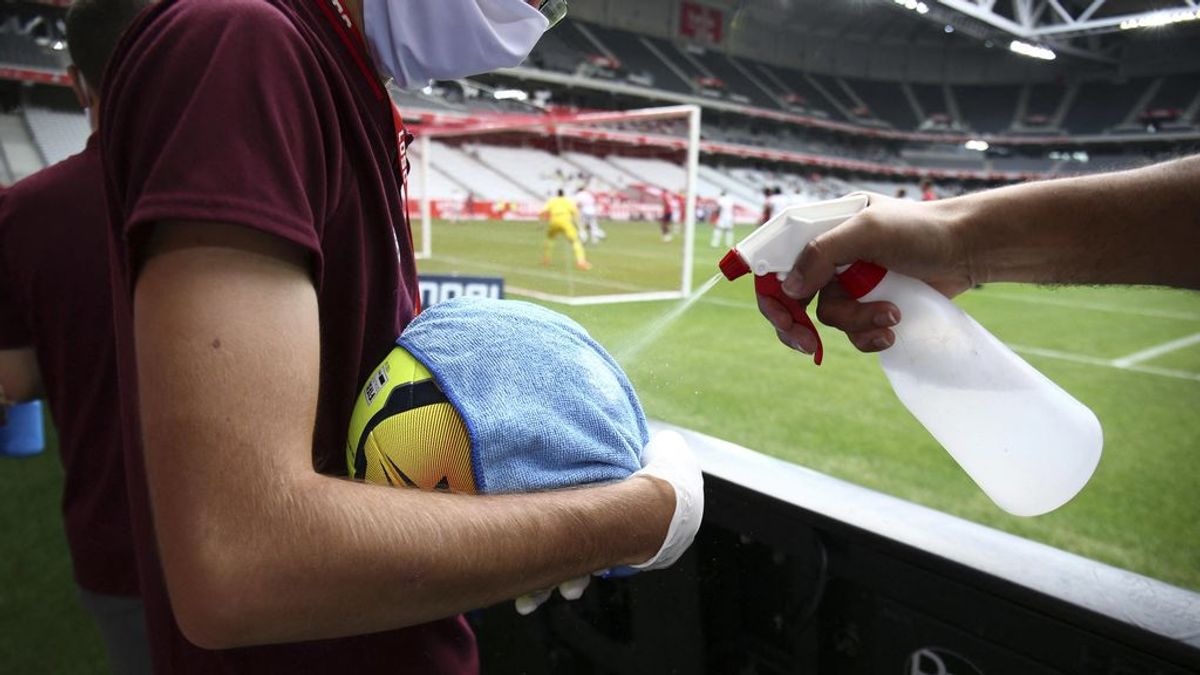 Dos operarios desinfectan un balón en un partido de fútbol.