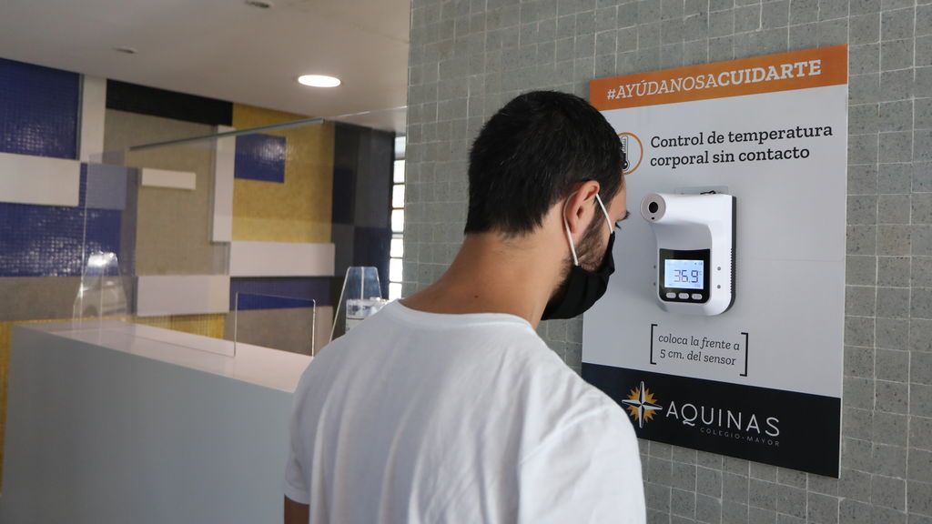 Un estudiante se toma la temperatura en un termómetro colocado en las instalaciones de un colegio mayor.