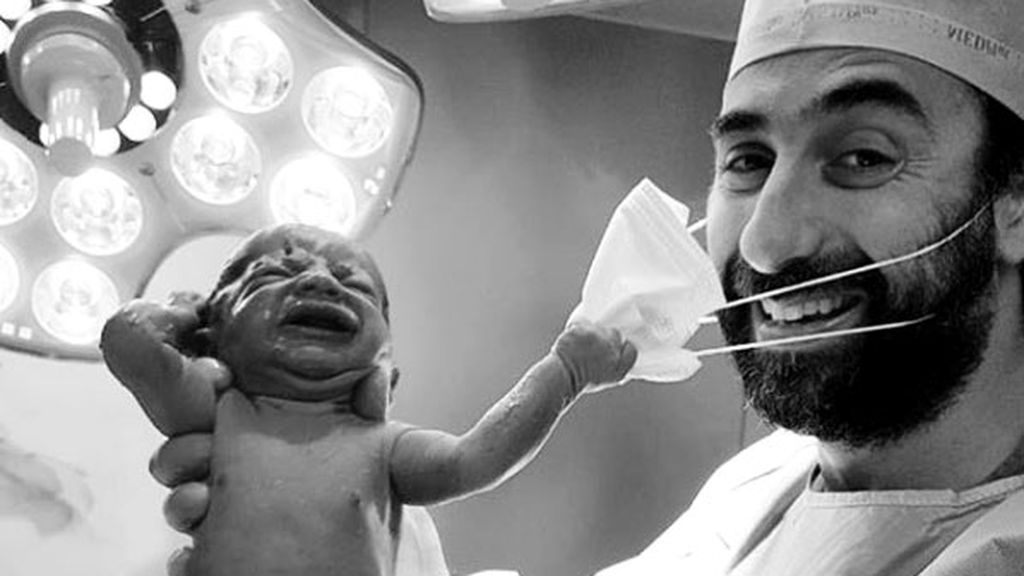 Un bebé recién nacido tira de la mascarilla del médico Un bebé recién nacido tira de la mascarilla del médico