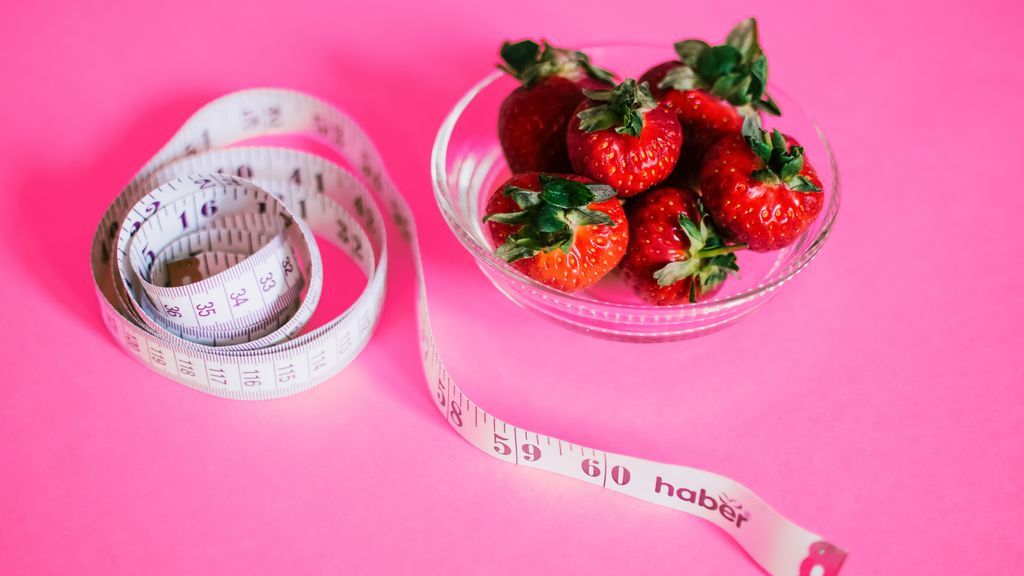 Fruta en un vaso, pesas y una cinta para medir el cuerpo.