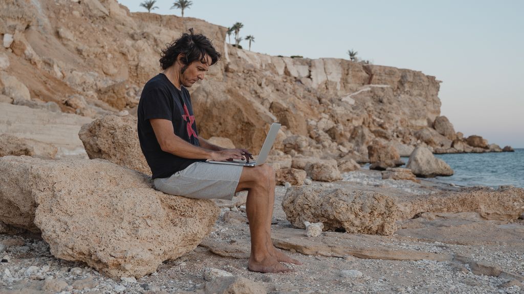 Un hombre trabajado con el ordenador desde la playa.