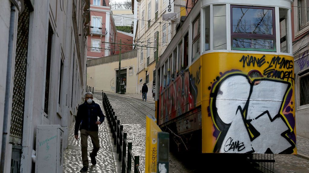 Un hombre con mascarilla junto a un tranvía de Lisboa