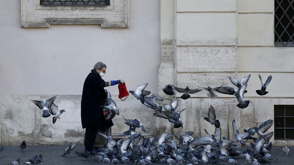 Una mujer con mascarilla da de comer a las palomas en Roma