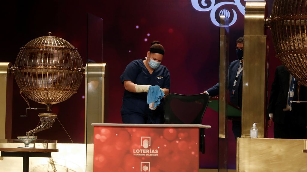 Una operaria del servicio de limpieza desinfecta el puesto del personal responsable del sorteo