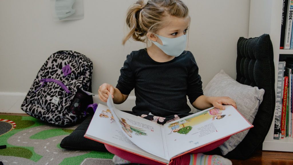 Una niña con mascarilla leyendo