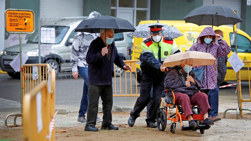Un mossos d'Esquadra ayuda a entrar al colegio electoral Centre Cívic Nord a una señora en silla de ruedas