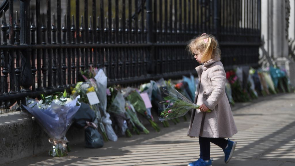 Una niña se dispone a colocar flores a la puertas del Palacio de Buckingham de Londres