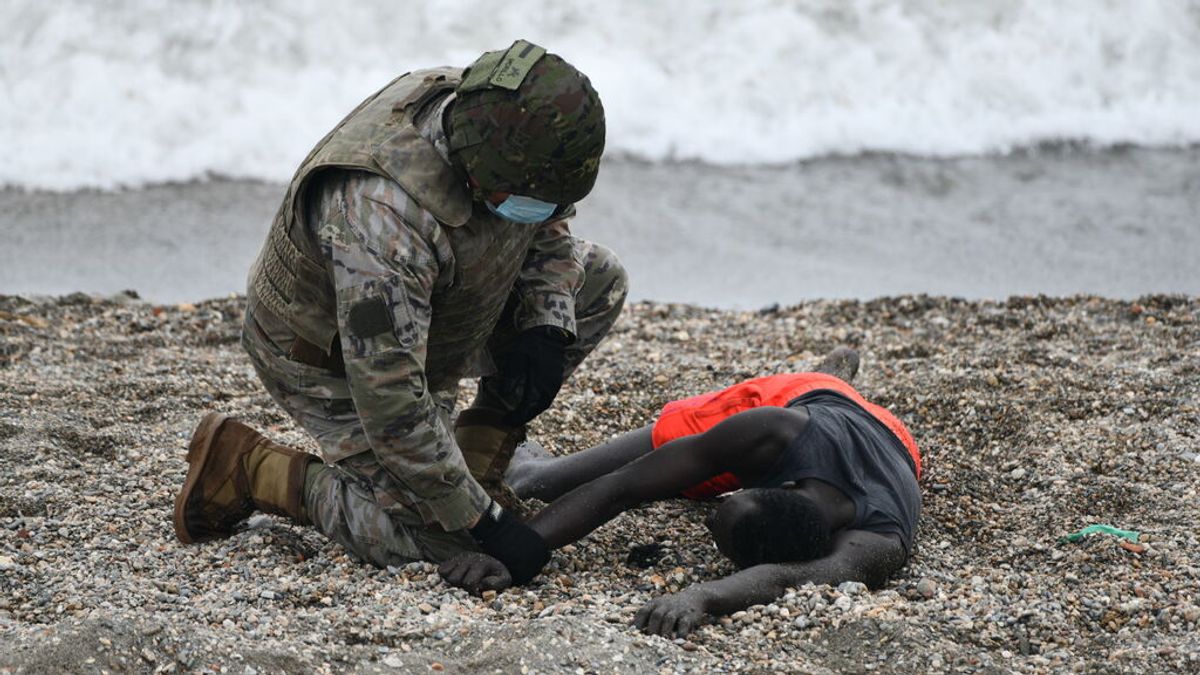 Un militar del ejército español ayuda a una persona tumbada en la orilla tras alcanzar Ceuta desde Marruecos. Un militar del ejército español ayuda a una persona tumbada en la orilla tras alcanzar Ceuta desde Marruecos.
