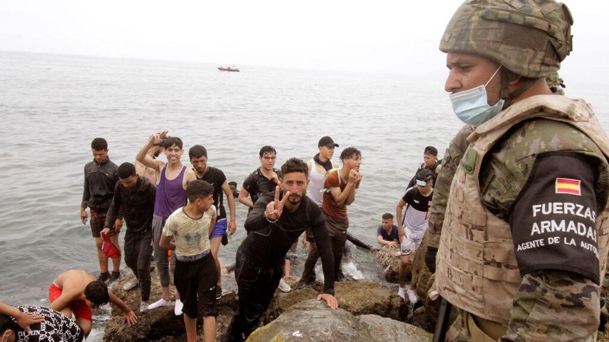 Un soldado del Ejército de Tierra observa como un grupo de inmigrantes escalan las rocas