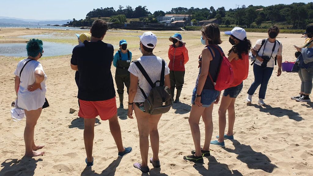 Turistas escuchan las explicaciones de las mariscadoras en la playa
