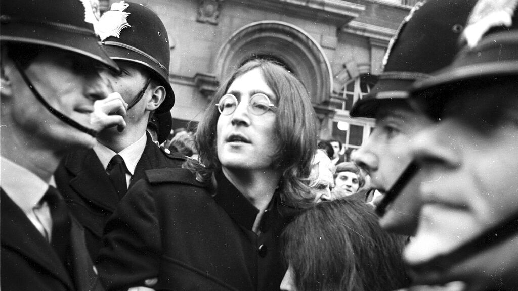 John Lennon protegiendo a Yoko Ono de la multitud a la salida de los juzgados.