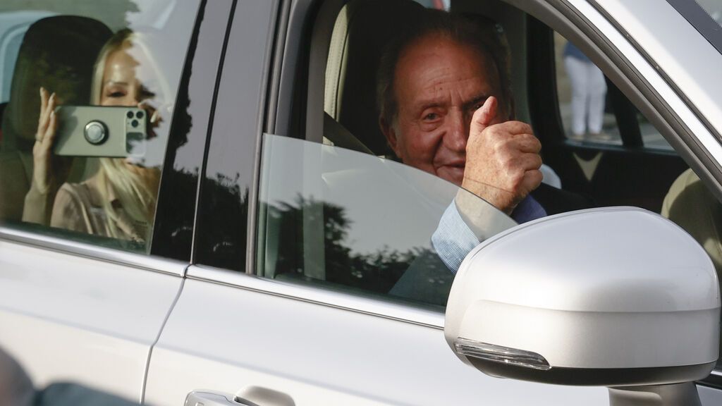 El rey Juan Carlos I y Cristina Franze, en el asiento trasero, saludan desde el coche camino a Sanxenxo