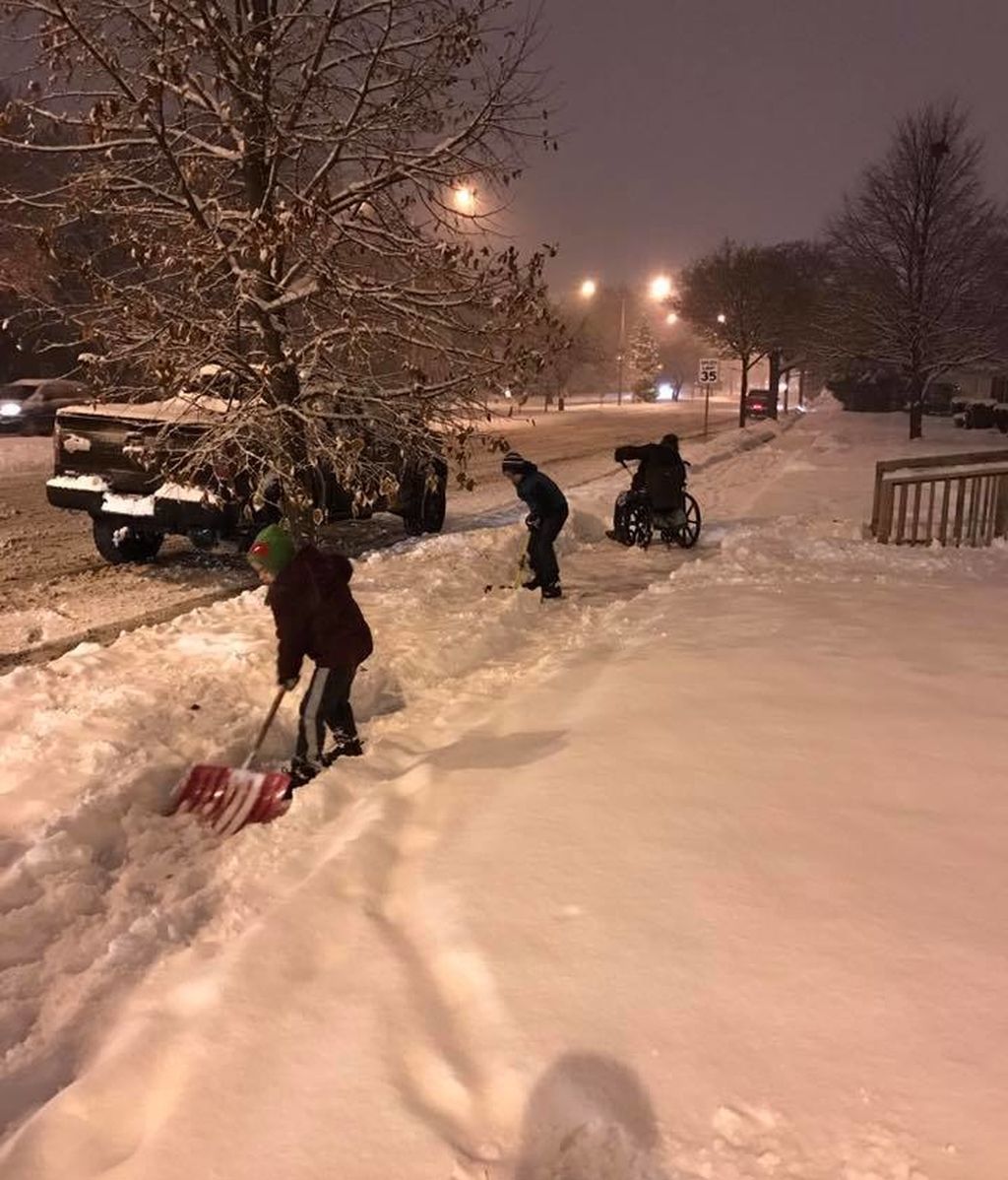 Sus hijos se bajan del coche para ayudar a un hombre en silla de ruedas a quitar la nieve