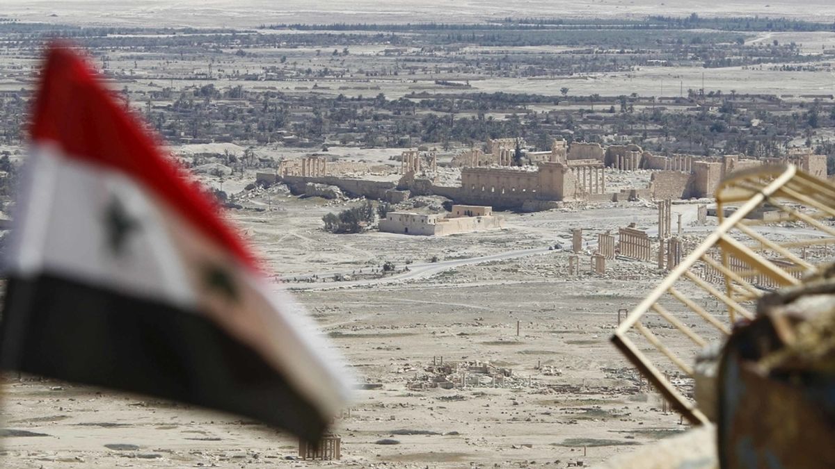 Una bandera nacional siria revolotea con las ruinas de la histórica ciudad de Palmira al fondo