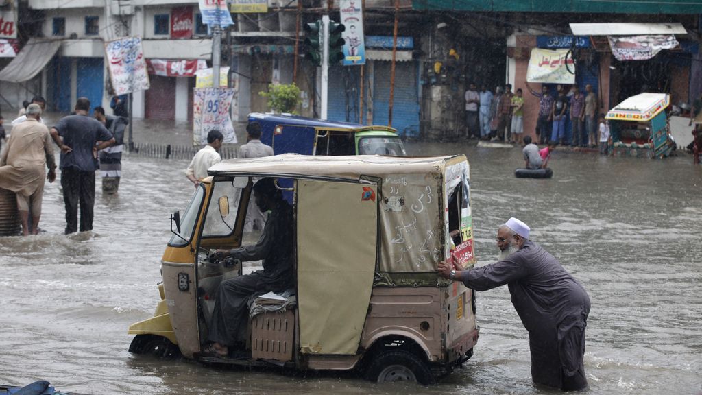 Un hombre empuja un auto rickshaw en medio del agua
