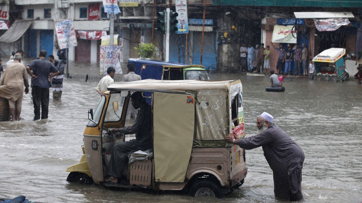 Un hombre empuja un auto rickshaw en medio del agua