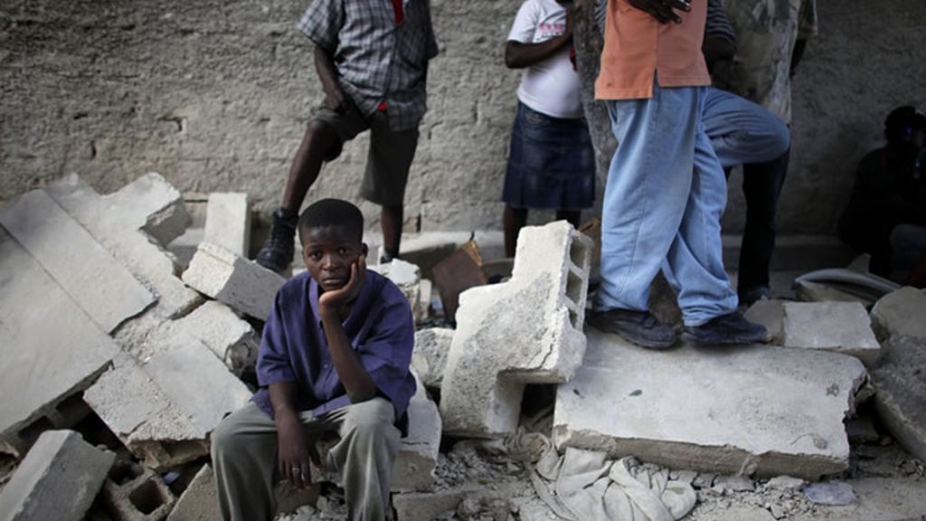 Un niño, desolado, sentado en las ruinas de la escuela
