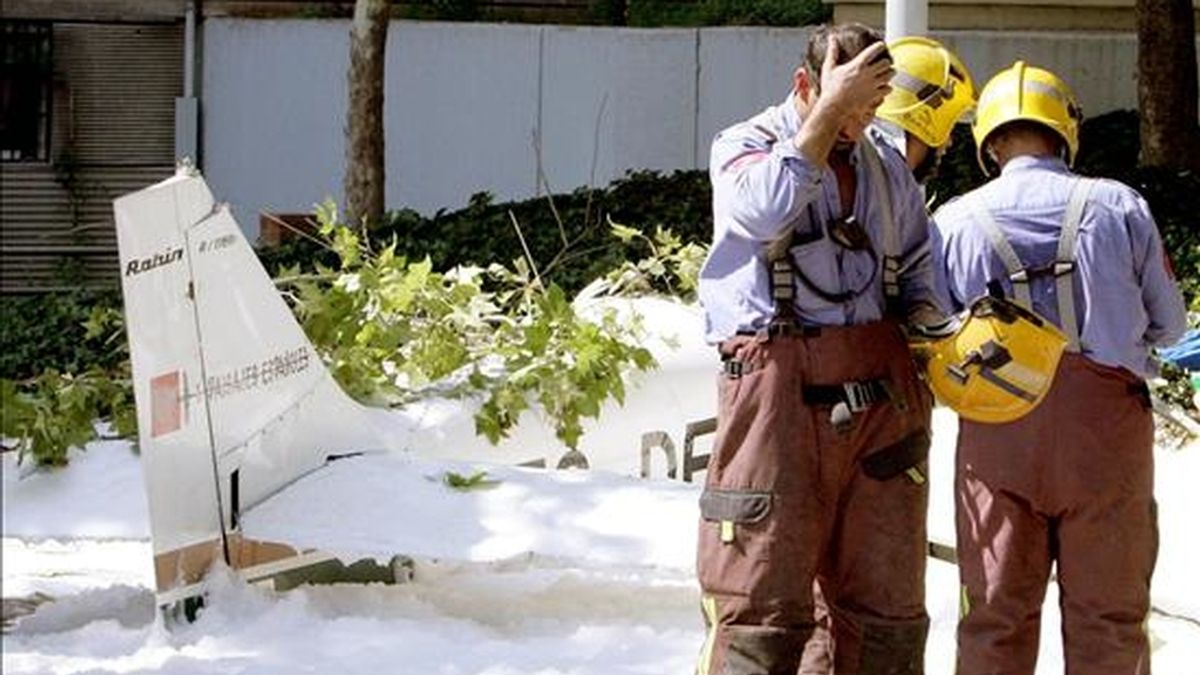 Un grupo de bomberos conversa en el casco urbano de la localidad de Badia del Vallés junto a los restos de una avioneta siniestrada en 2005. EFE/Archivo