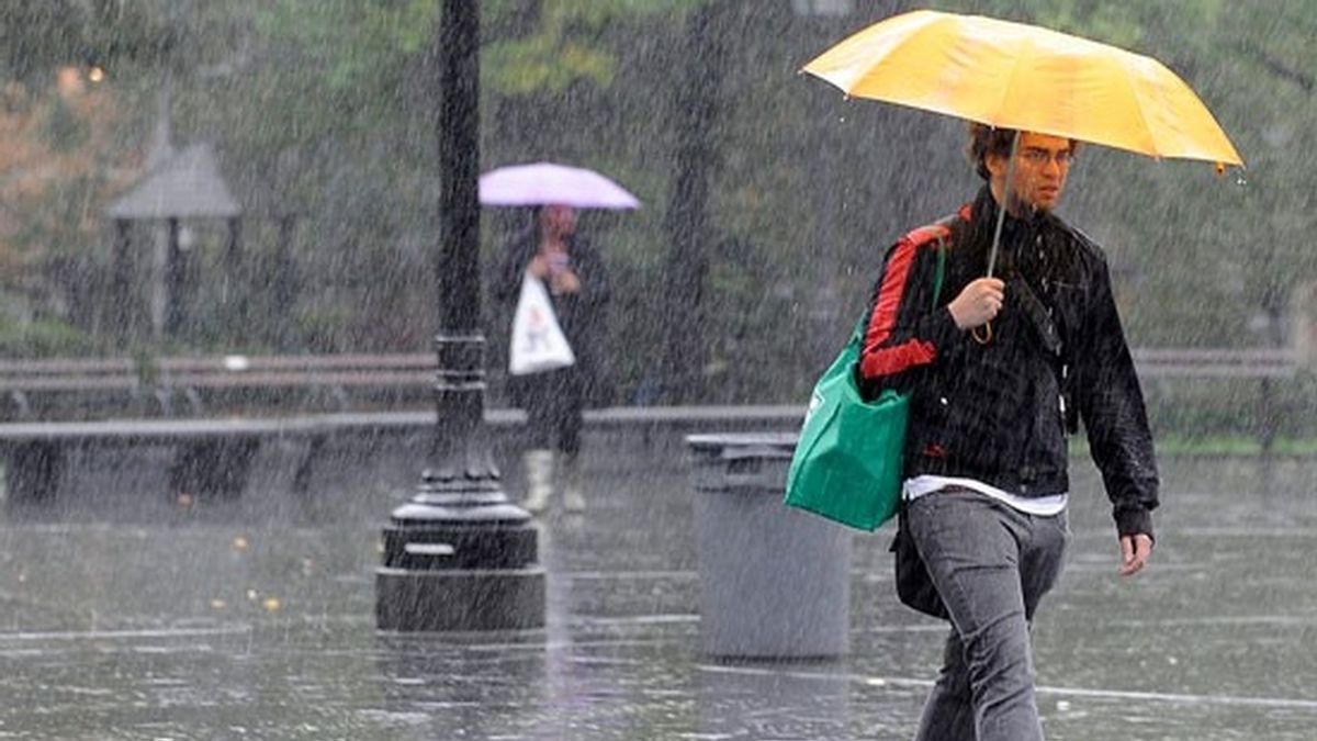 Un joven se resguarda bajo su paraguas de la fuerte lluvia