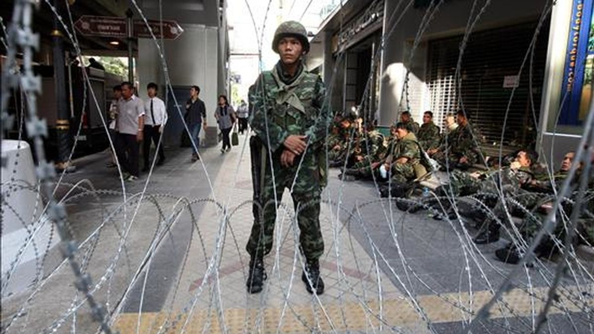 Trabajadores pasan junto a militares tailandeses armados hoy, en el distrito financiero de Bangkok (Tailandia) en donde tomaron posiciones para impedir que lo paralicen los miles de manifestantes antigubermanentales que exigen la disolución del Parlamento. EFE