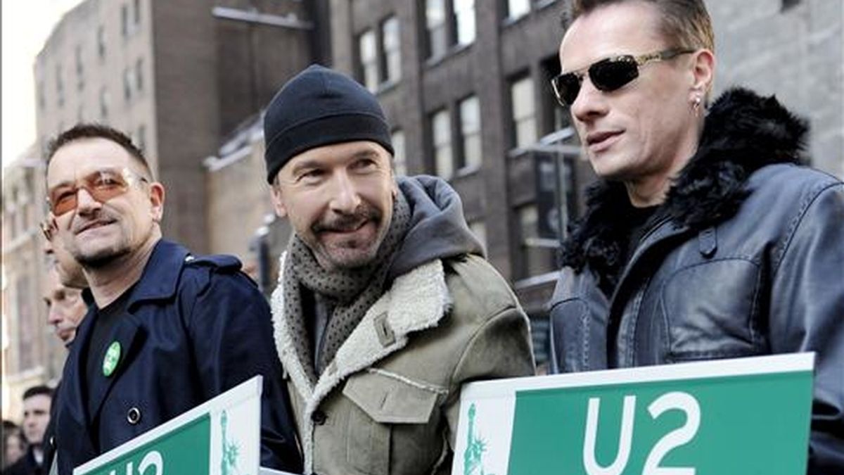Los componentes de la banda de música U2: Bono, The Edge, y Larry Mullen Jr., posan con copias de señales viarias que indican la "Via U2" el pasado 3 de marzo en Nueva York (Estados Unidos). EFE/Archivo