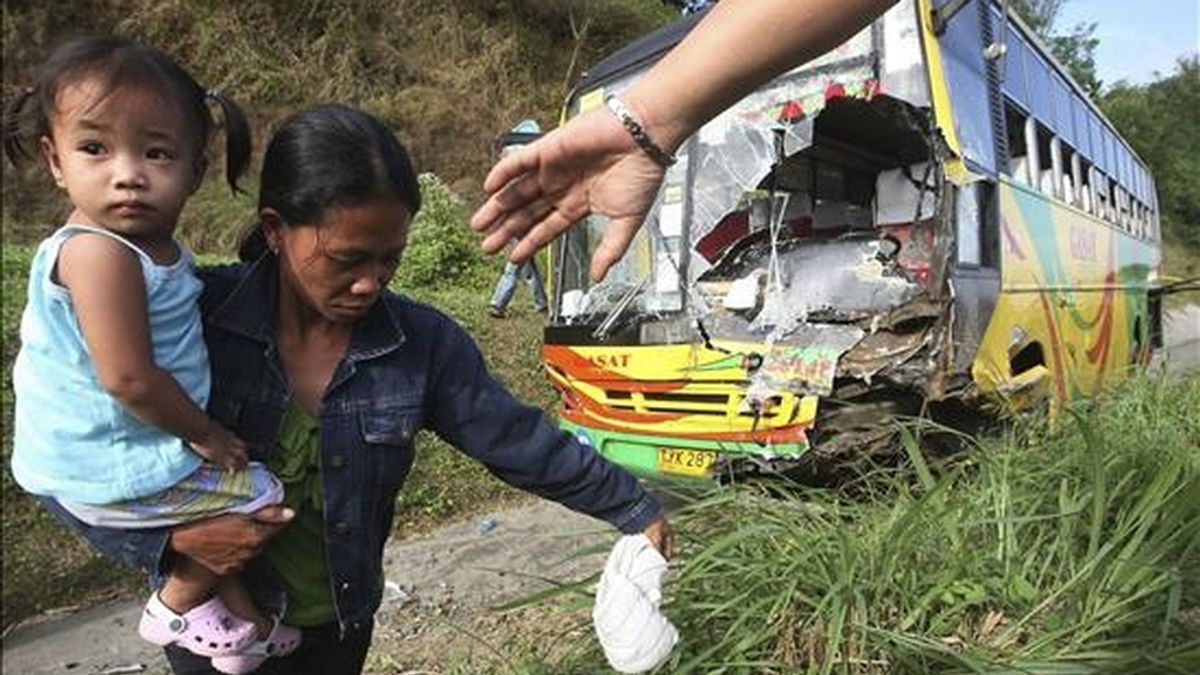 Una mujer camina con su hija en brazos tras sobrevivir a un accidente entre un autobús y un todoterreno en la provincia de Batangas al sur de Manila (Filipinas). EFE