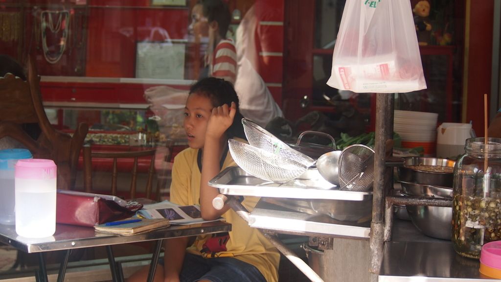 Adolescente estudiando en el puesto de comida de su madre