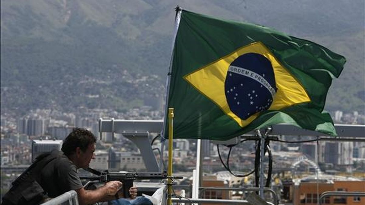 Un policía monta guardia junto a la bandera de Brasil en el punto más alto del Complexo do Alemao para simbolizar la toma de ese conjunto de favelas en Río de Janeiro (Brasil) que hasta esta mañana era dominado por narcotraficantes. EFE