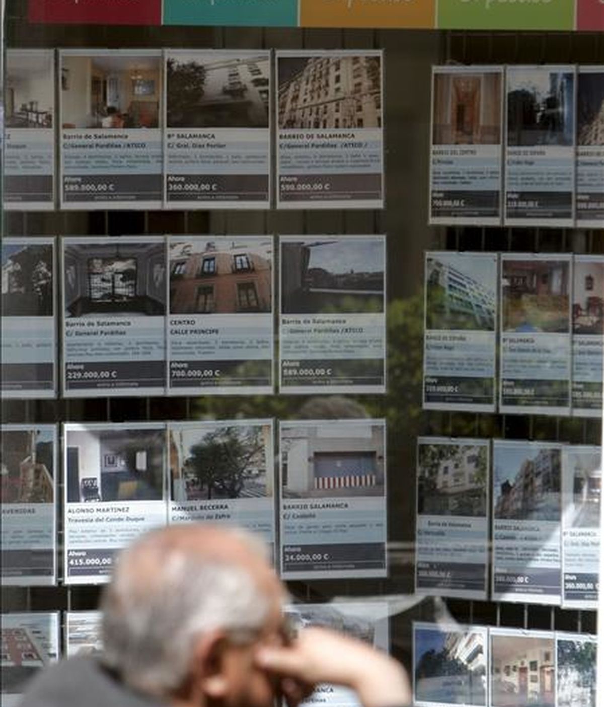 Un hombre sentado junto a una inmobiliaria que muestra en su escaparate las numerosas ofertas de venta y alquiler de inmuebles, en Madrid. EFE/Archivo