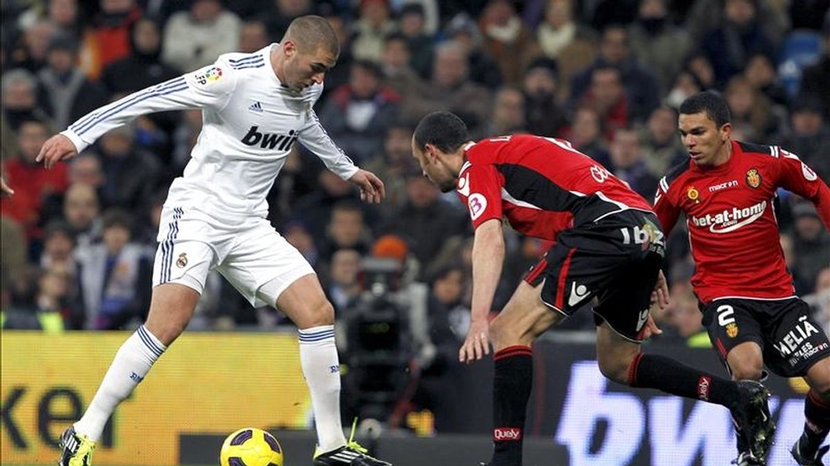 El delantero francés del Real Madrid Karim Benzema (i) encara con el balón a los defensas del RCD Mallorca Iván Ramis (c) y el brasileño Edson Ramos "Ratinho" durante el partido correspondiente a la vigésima jornada del Campeonato Nacional de Liga de Primera División que enfrentó a ambos equipos en el estadio Santiago Bernabéu. EFE