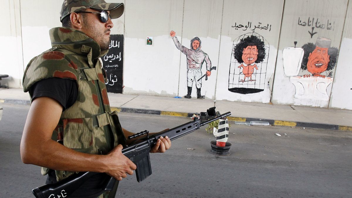 Un rebelde libio en un punto de control con caricaturas de Gadafi