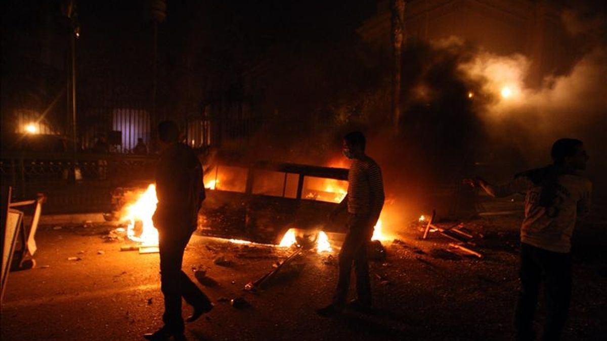 Manifestantes caminan frente a un vehículo en llamas tras las protestas que estallaron al término de las oraciones del viernes en el centro de El Cairo. EFE