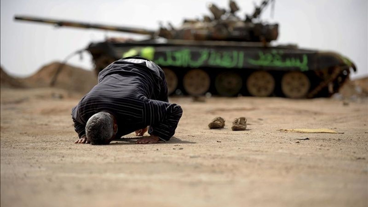 Un insurgente libio reza junto a los restos de un tanque destruído en las proximidades de Ajdabiya, Libia. EFE/Archivo