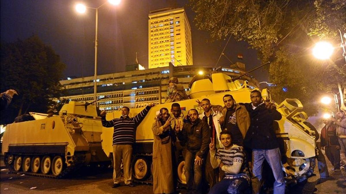 Manifestantes muestran la señal de la victoria junto a varios vehículos armados que permanecen frente al edificio de la radio y televisión estatal luego de una serie de protestas que estallaron tras las oraciones del viernes en el centro de El Cairo. EFE