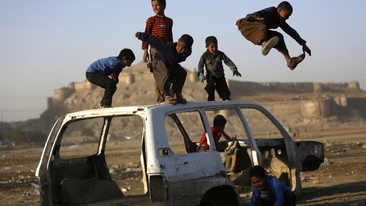 Niños afganos juegan en un coche destruído