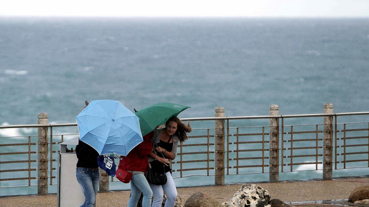 Tres turistas se protegen del fuerte viento y las precipitaciones en San Sebastián