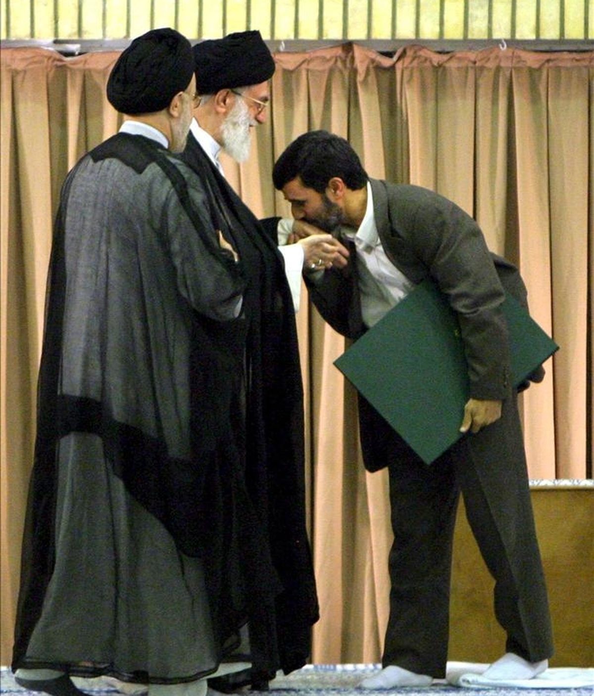 El presidente de Irán, Mahmud Ahmadineyad (d), besando la mano del líder supremo iraní, el ayatolá Alí Jameneí (c), durante una ceremonia en una mezquita de Teherán en 2005. EFE