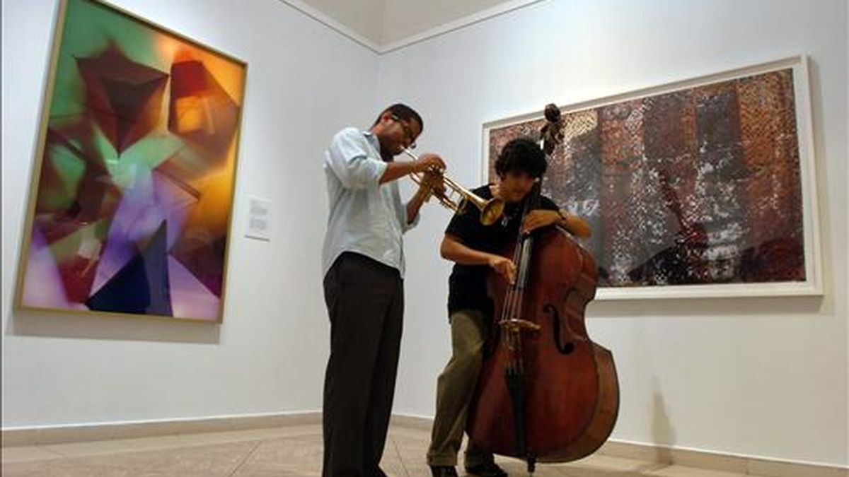 Dos músicos tocan sus instrumentos junto a las obras "La Colonia Penal" (d), del vietnamita Dinh Q. Le, y "Teepee", del estadounidense William T. Hillman, exhibidas en el Museo Nacional de Bellas Artes, como parte de la Décima Bienal de Arte de La Habana (Cuba). EFE