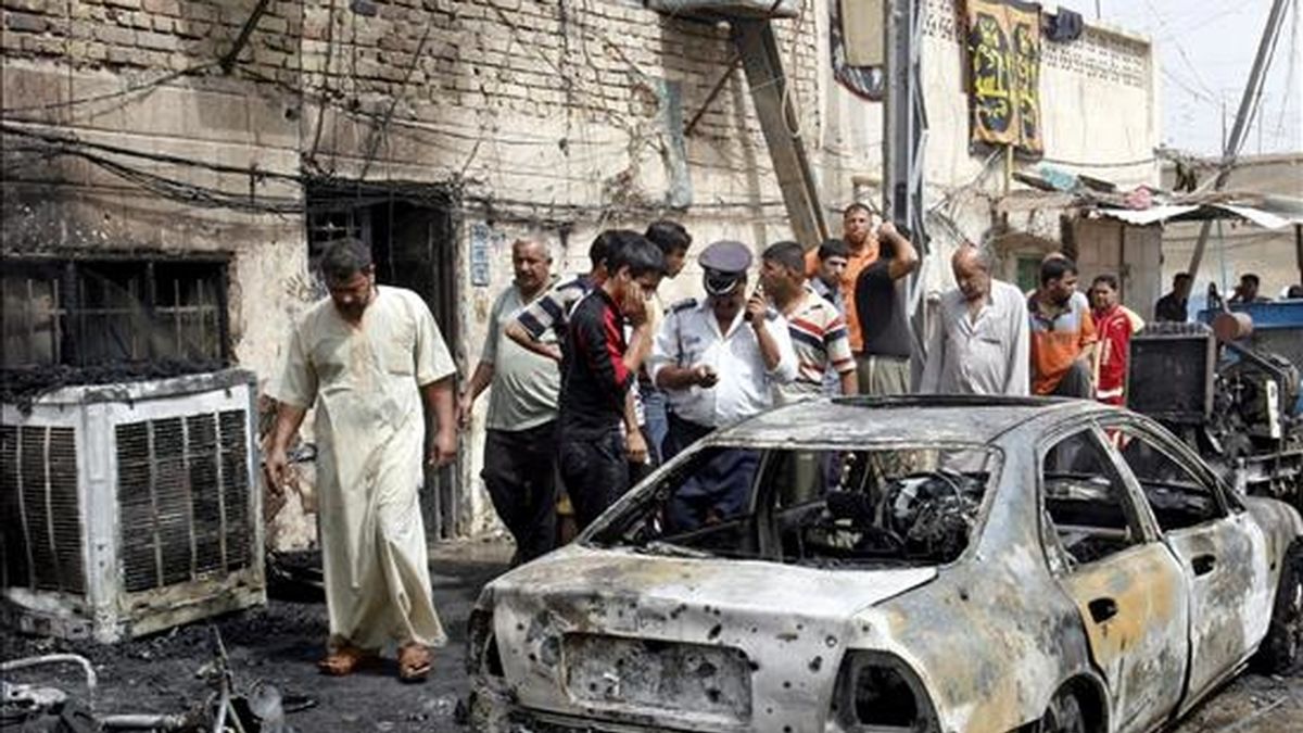 Un grupo de personas observa un coche destrozado tras un atentado en el distrito de Sader en Bagdad. EFE/Archivo