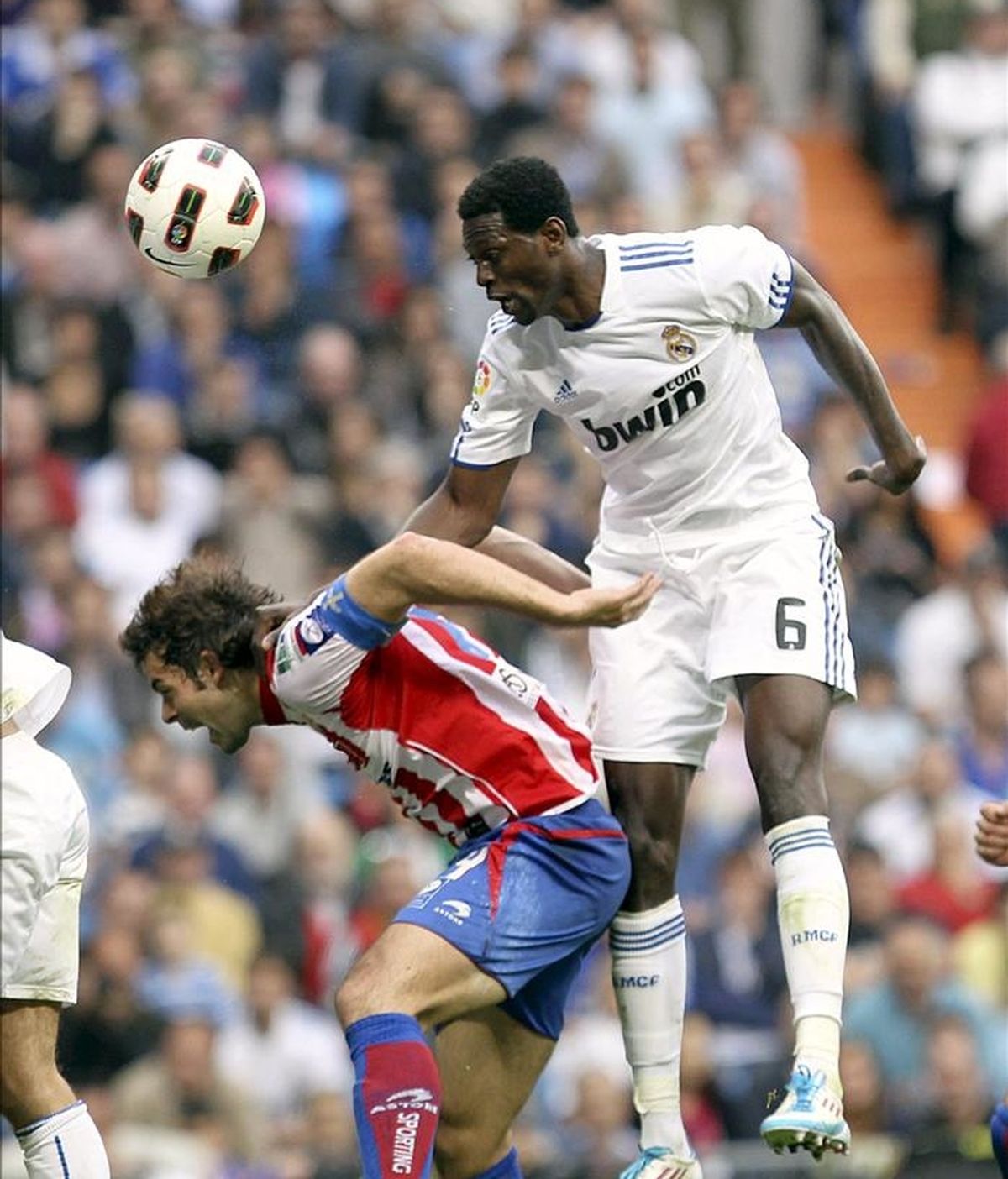 El delantero togolés del Real Madrid Emmanuel Adebayor (d) remata de cabeza un balón ante el defensa del Sporting de Gijón Iván Hernández durante el partido correspondiente a la trigésima jornada de Liga de Primera División que ha enfrentado a ambos equipos esta tarde en el estadio Santiago Bernabéu. EFE