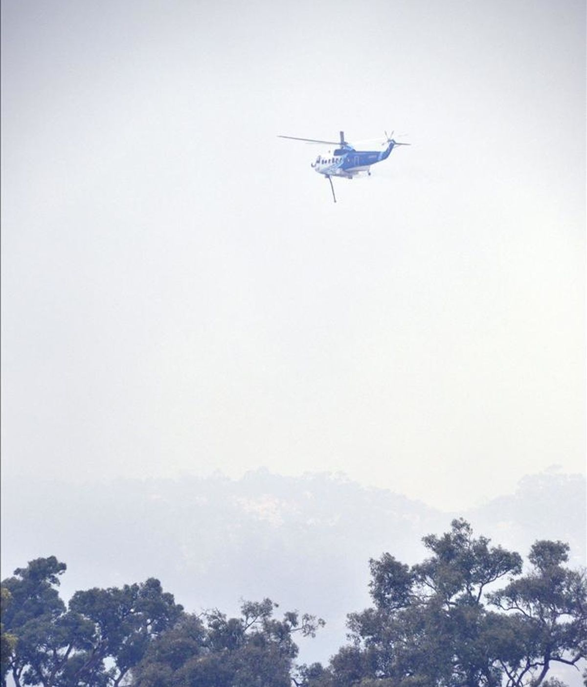 Un helicóptero lucha hoy contra el rápido avance de un incendio fuera de control cerca de Perth, ubicada en el estado de Australia Occidental. EFE