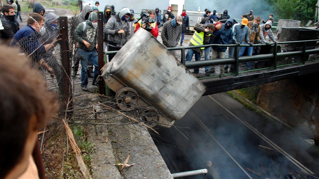 Un grupo de mineros lanza desde un puente a la carretera contenedores incendiados, en las inmediaciones del pozo Barredo, de Hunosa