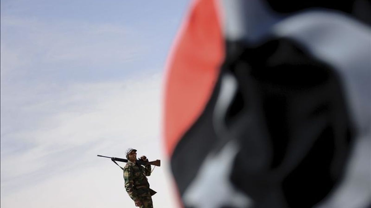 Una bandera libia pre-Gadafi situada ante un soldado libio vigilante desde un punto de control, en la localidad de Ajdabiya. EFE/Archivo