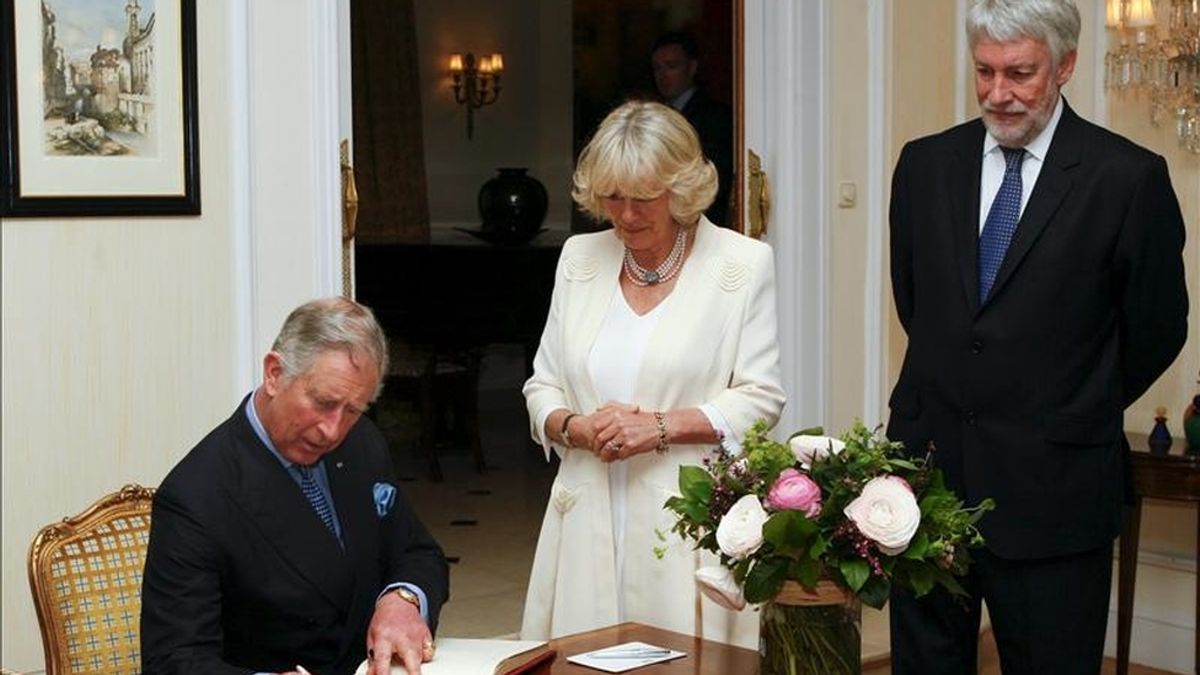 El príncipe Carlos de Inglaterra ante su esposa, Camila, Duquesa de Cornualles, y el embajador británico en España, Giles Paxman (d) firma en el libro de la residencia del Embajador, en Madrid. EFE