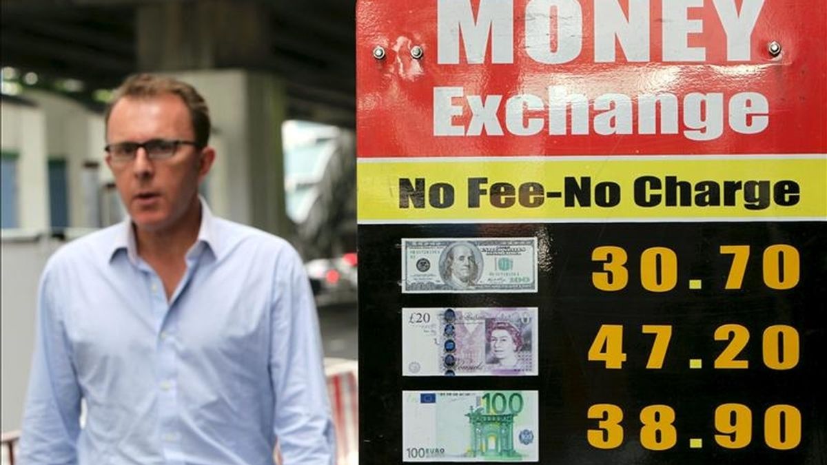 Un hombre camina junto a un tablero con los valores de distintas divisas en el distrito financiero de Bangkok. EFE/Archivo