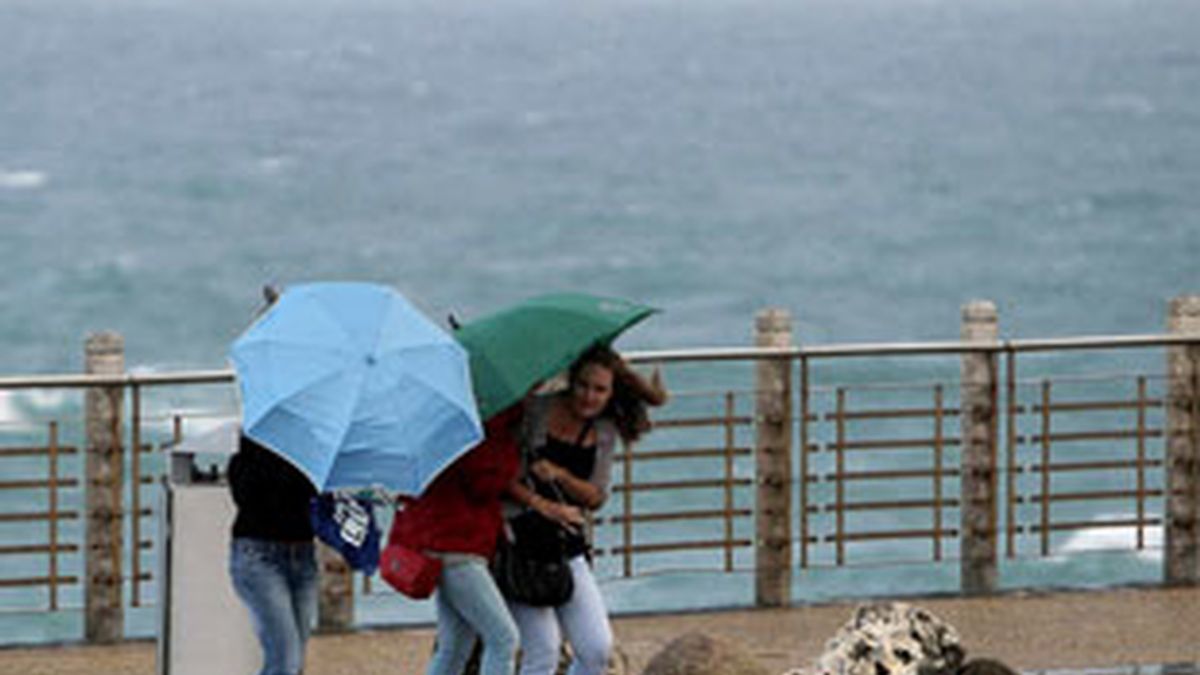 Tres turistas se protegen del fuerte viento y las precipitaciones en San Sebastián. Foto: EFE.