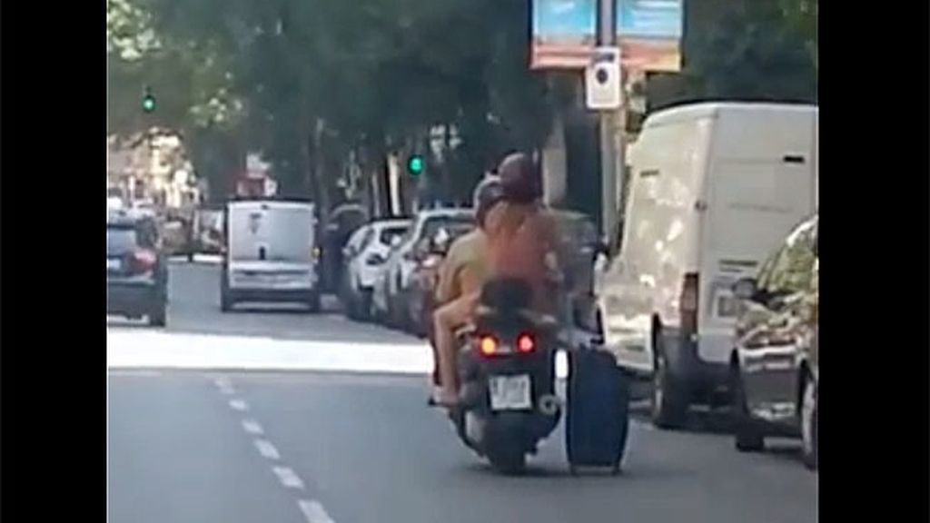Una pareja arrastra una maleta desde una moto por las calles de Barcelona