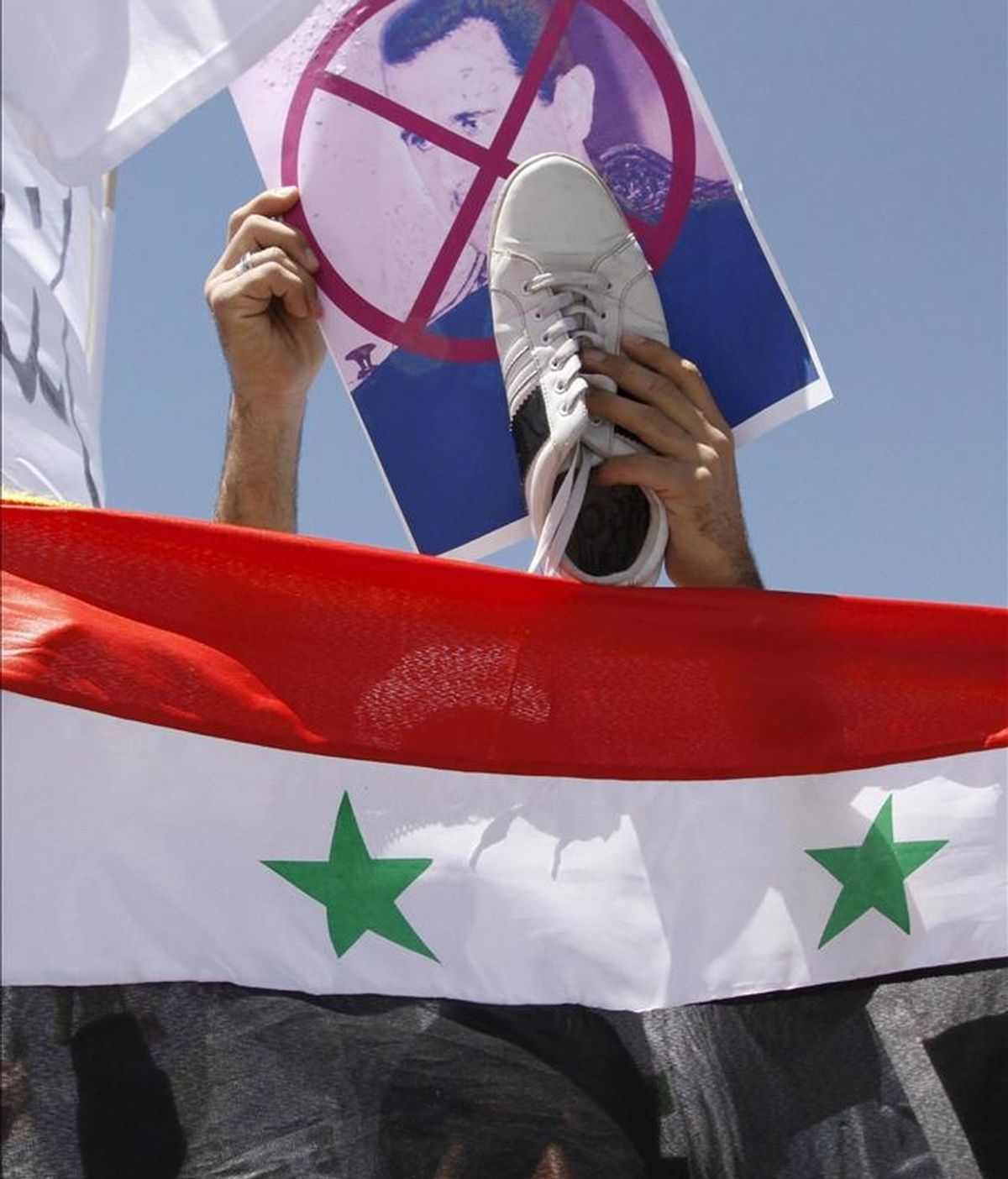 Un sirio residente en Jordania sostiene un retrato del presidente de Siria, Bachar al Asad, y un zapato sobre la bandera nacional durante una manifestación frente a la embajada siria en Amán hoy. EFE